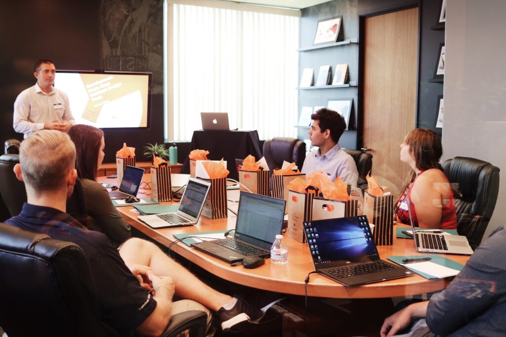 A group of employees gathered around a big conference table while looking at their laptops.