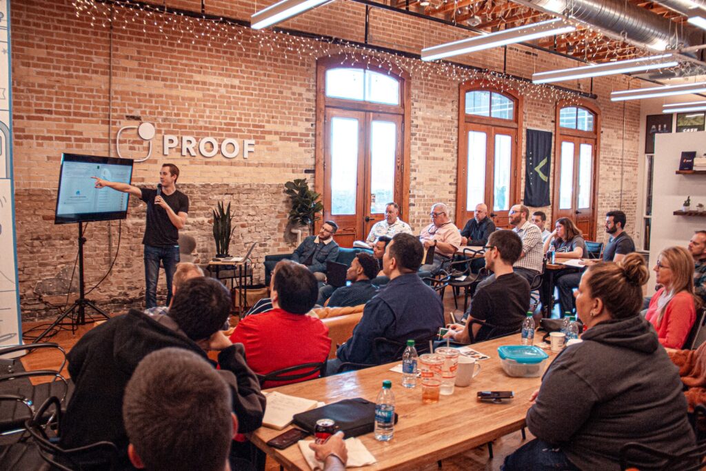A group of employees gathered around a wooden conference table while studying a projector screen that shows various data analytics.