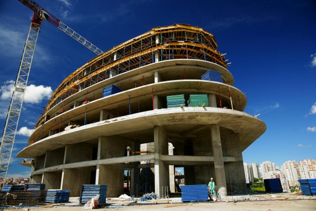 Low angle view of a circular building under construction with a crane, clear blue sky.