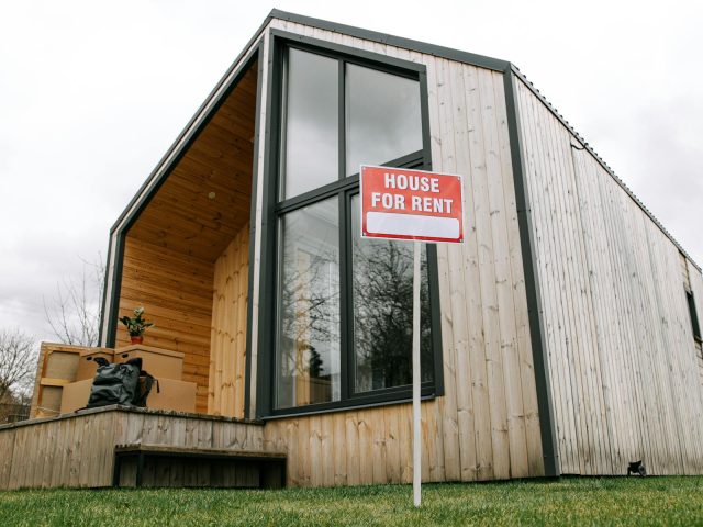 Low-angle view of a modern wooden house with a 'House for Rent' sign, showcasing contemporary architecture.